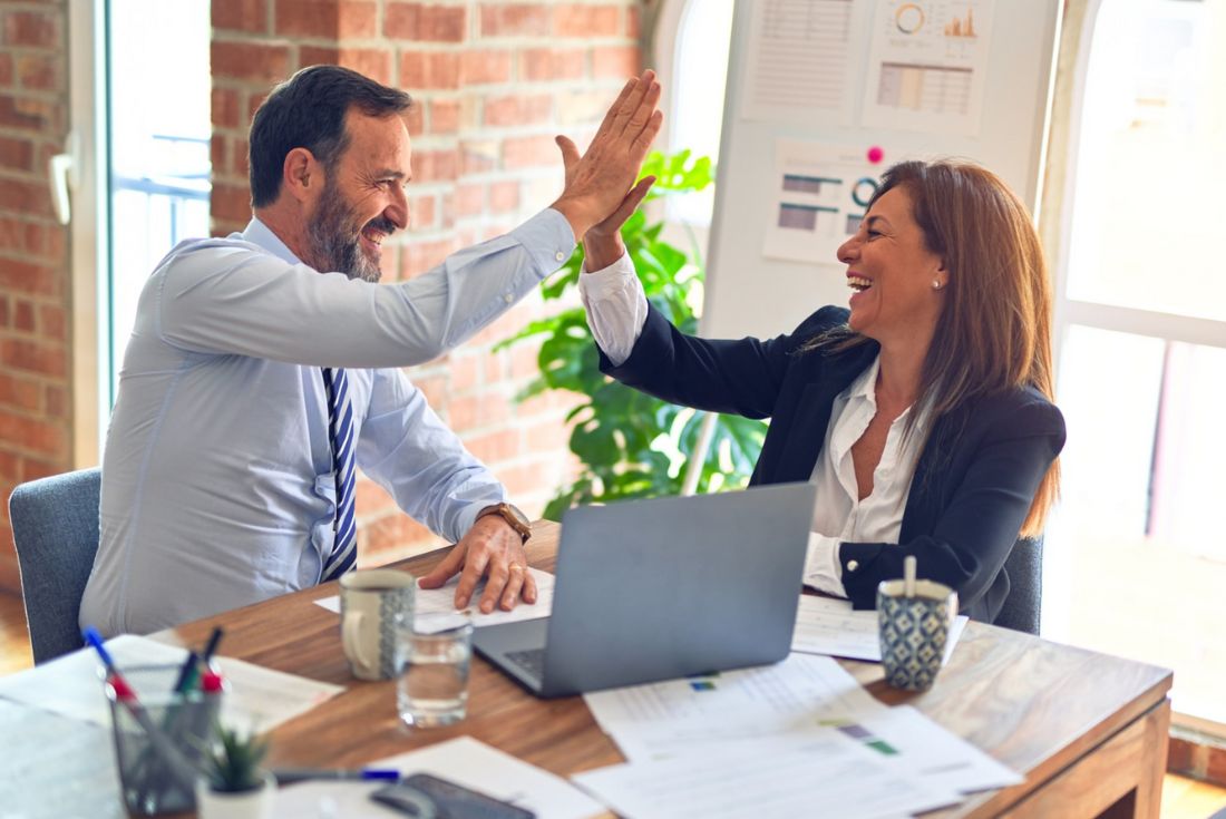 Two professionals high-fiving each other over a desk