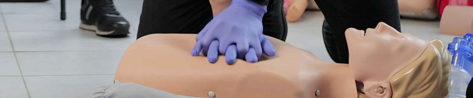 Close-up of hands wearing purple gloves performing chest compressions on a CPR training mannequin during a first aid class.