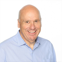Headshot of a smiling bald man in a light blue button-up shirt, photographed against a clean white background.