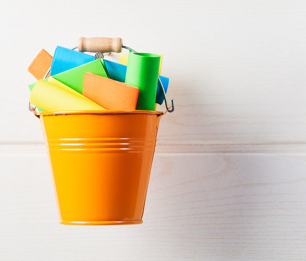 Bucket list concept. Orange bucket with colorful paper notes hanging on white wooden wall