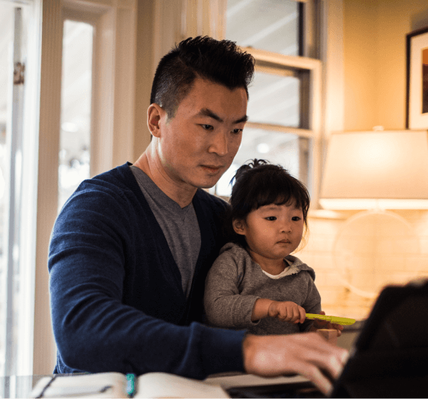 A father sits with his daughter on his lap while working on a computer.