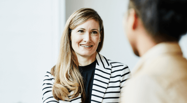 A business woman interacts with a person in the foreground.