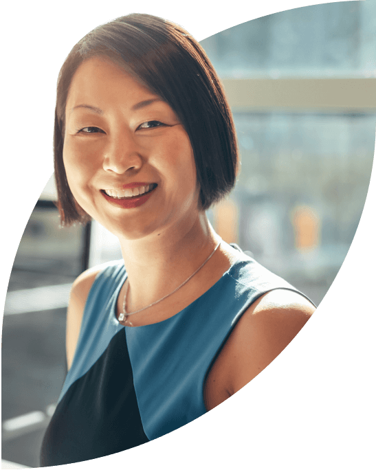 Smiling businesswoman looking towards the viewer, in a well-lit office space with large windows.