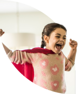 Petite fille vêtue d’une cape de super-héros, bras tendus, riant joyeusement.