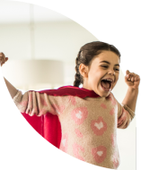 Little girl dressed up in a superhero cape with arms outstretched, laughing happily.