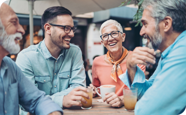 Groupe d’amis souriant et discutant à une table dans le patio d’un café en plein air.