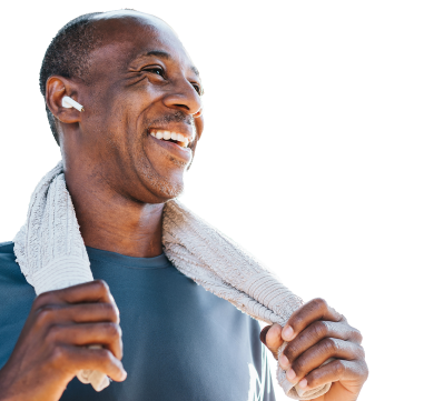 Un homme souriant et athlétique au crâne rasé portant un écouteur, enroule une serviette autour de son cou.