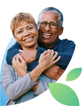 Older, vibrant-looking couple with close-cropped hairstyles embrace each other while looking at the camera and laughing.