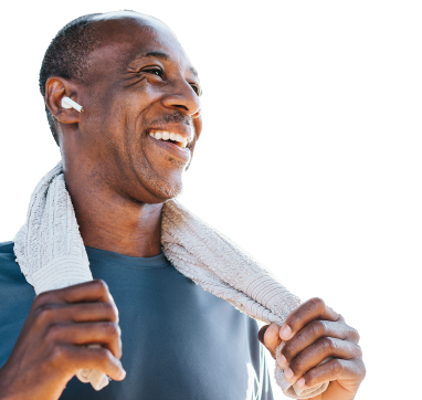 Un homme souriant et athlétique au crâne rasé portant un écouteur, enroule une serviette autour de son cou.