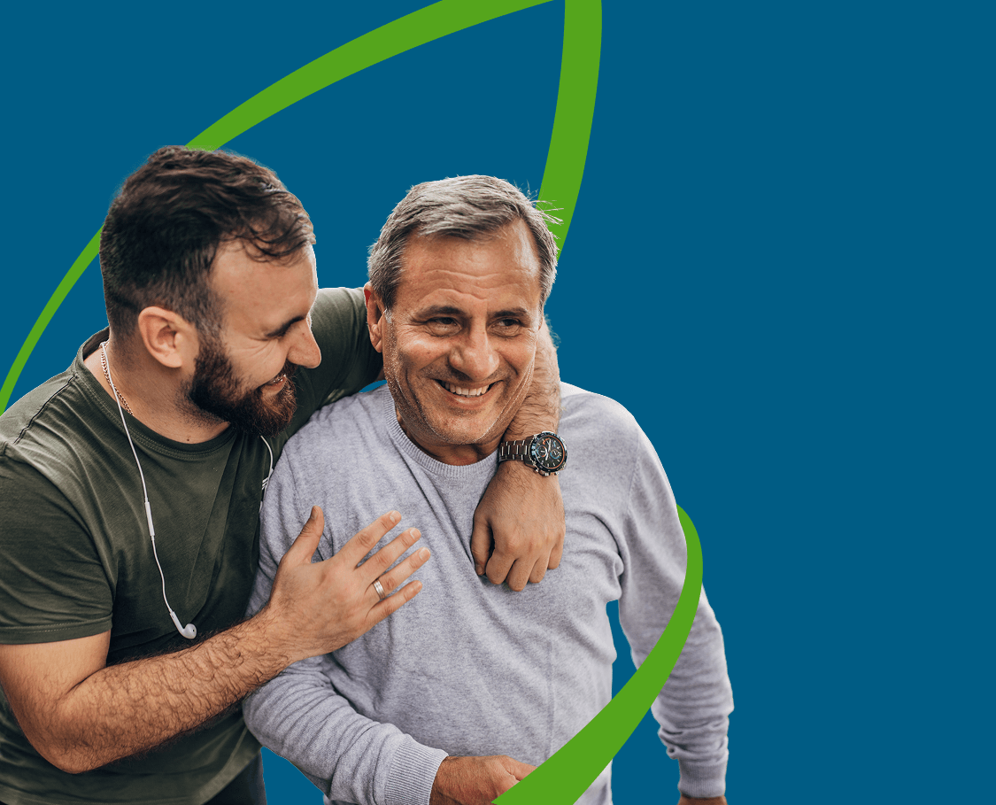 Un homme, les écouteurs autour du cou, a le bras autour des épaules de son père plus âgé; tous deux sourient et rient, tandis qu’une ligne verte formant la silhouette d’une feuille les entoure.